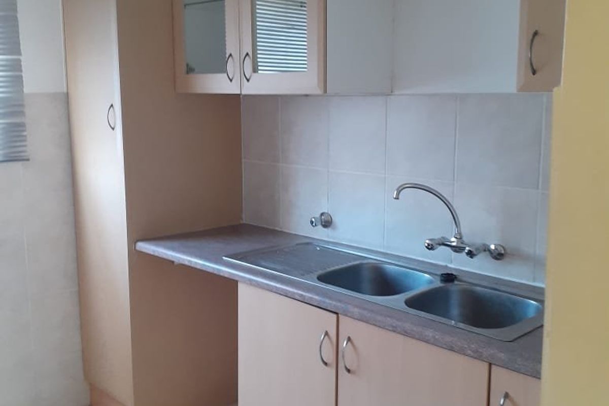 A functional kitchen featuring laminate cabinetry, a double bowl stainless steel sink, tiled splashback, and tiled flooring.