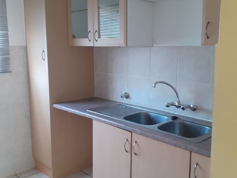 A functional kitchen featuring laminate cabinetry, a double bowl stainless steel sink, tiled splashback, and tiled flooring.