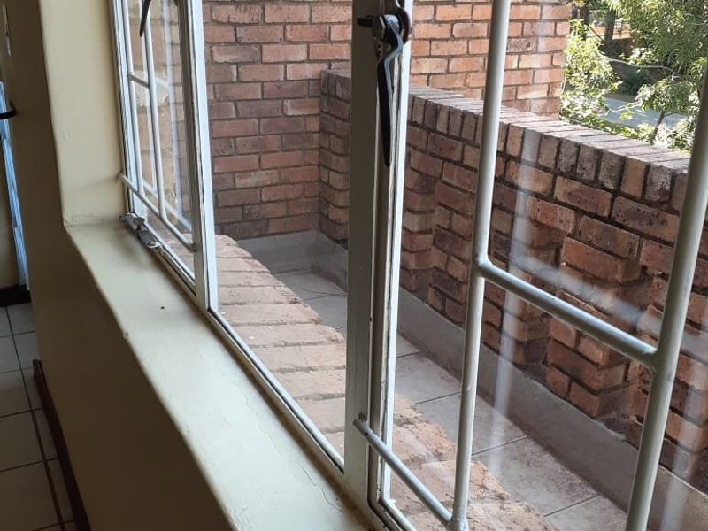 A view from inside looking out onto a private balcony featuring brick walls and tiled flooring, accessible through large casement windows.
