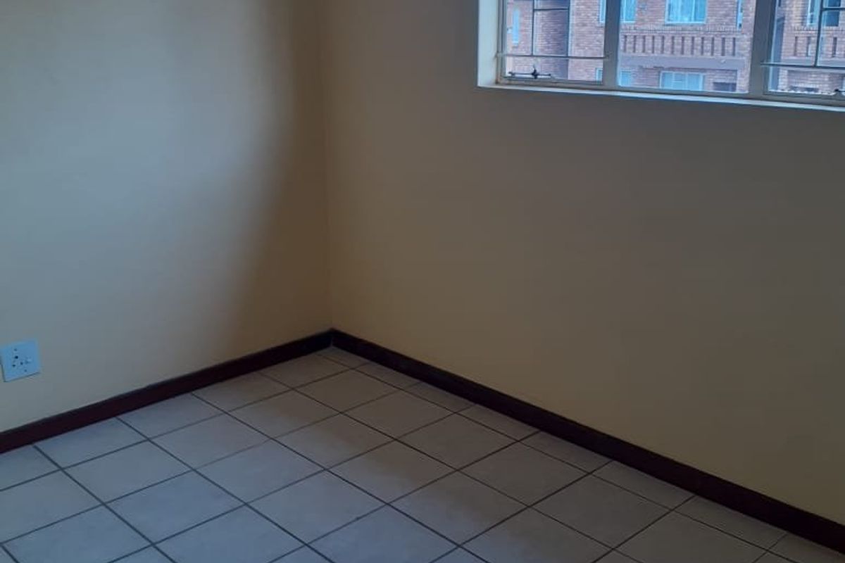 An empty bedroom featuring neutral walls, tiled flooring, and a window fitted with security bars.