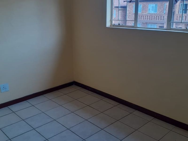 An empty bedroom featuring neutral walls, tiled flooring, and a window fitted with security bars.