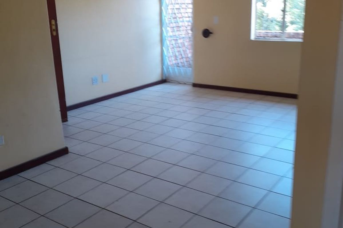 An empty, tiled living area featuring neutral walls, a security gate, and a window, providing a blank canvas for interior design.