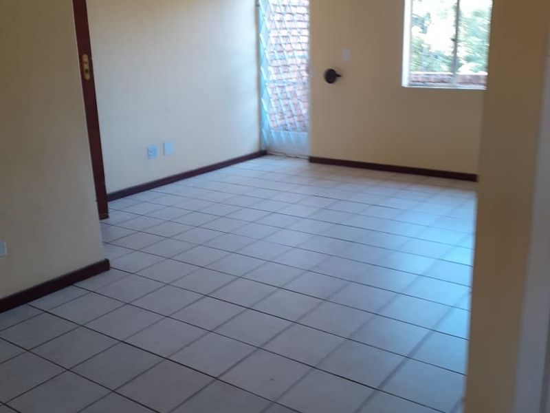 An empty, tiled living area featuring neutral walls, a security gate, and a window, providing a blank canvas for interior design.