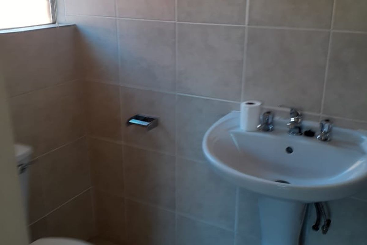 A functional bathroom featuring a pedestal basin, toilet, and neutral ceramic wall and floor tiling.
