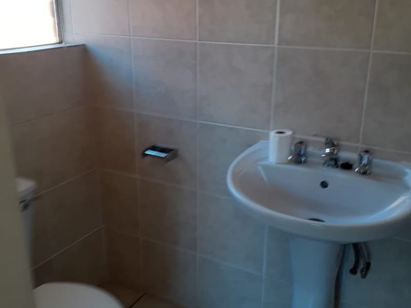 A functional bathroom featuring a pedestal basin, toilet, and neutral ceramic wall and floor tiling.
