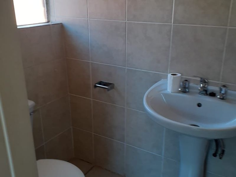 A functional bathroom featuring a pedestal basin, toilet, and neutral wall and floor tiling.