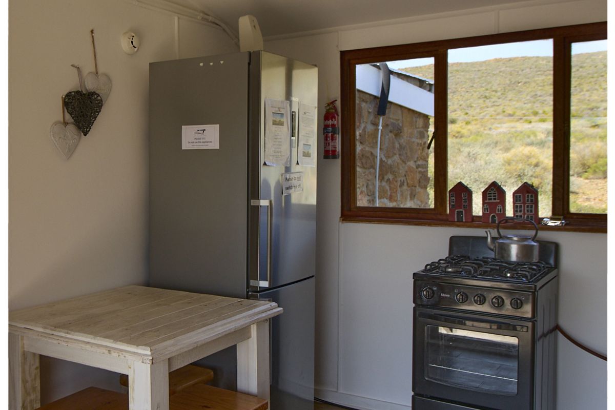 A compact kitchen area featuring a gas stove, oven, and refrigerator, with a window offering scenic rural views.