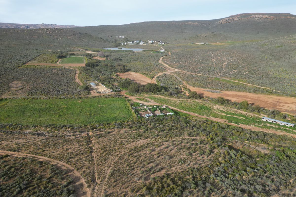 An aerial view of a large farm property featuring expansive agricultural land, dirt access roads, fenced paddocks, and various farm outbuildings.