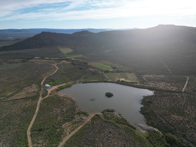 Aerial view of a vast farm property featuring a large dam, surrounding agricultural land, and mountain vistas in the distance.
