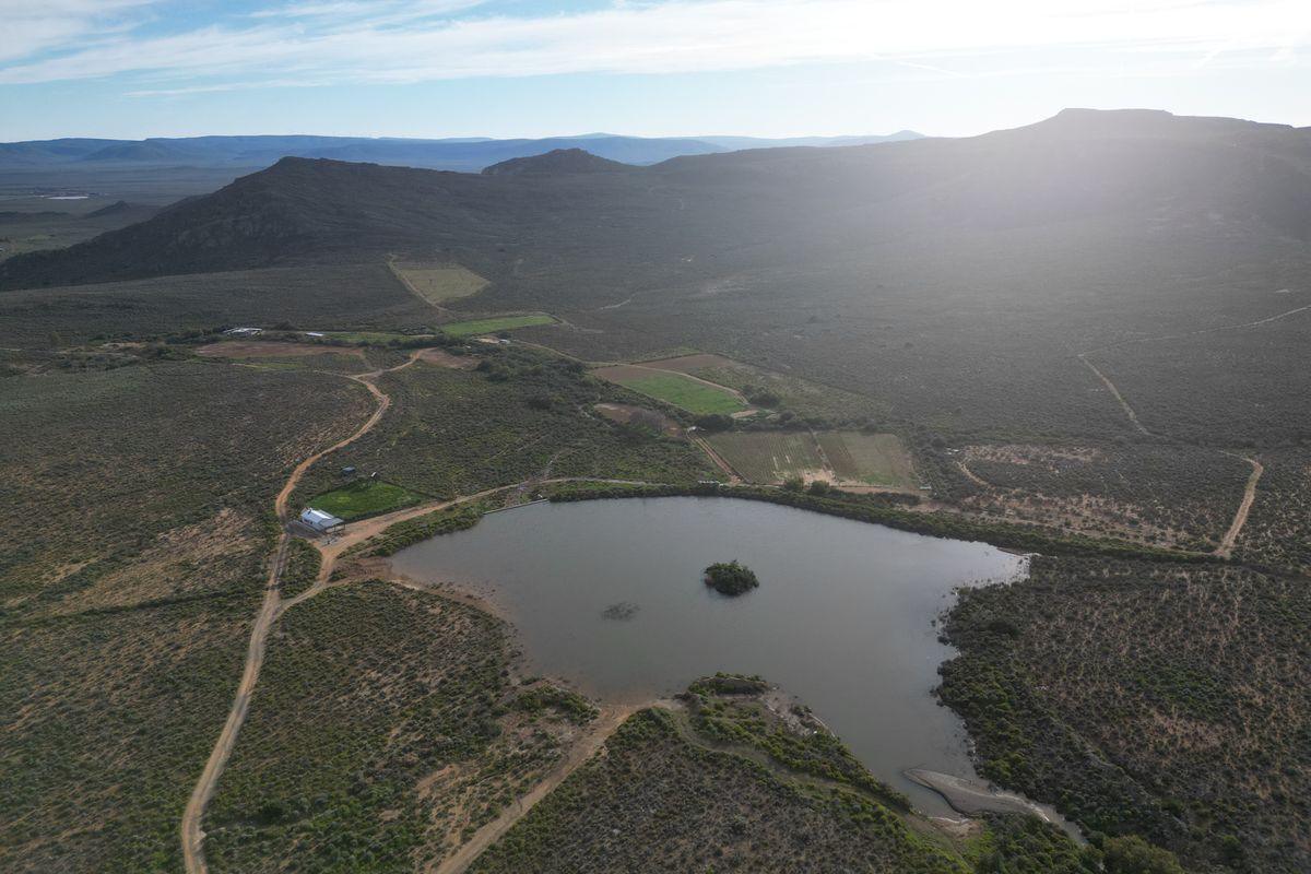 Aerial view of a vast farm property featuring a large dam, surrounding agricultural land, and mountain vistas in the distance.