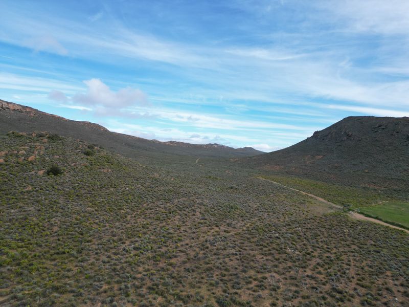 An aerial view of the expansive farm landscape featuring rolling hills, natural vegetation, and a dirt access road.