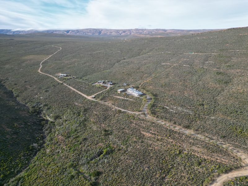 An aerial view of a rural farm property featuring multiple buildings, gravel access roads, and expansive natural landscape.