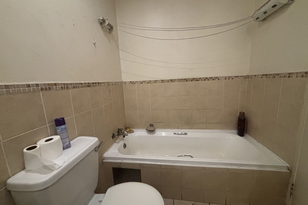 A functional bathroom featuring a built-in bathtub, ceramic tiling, and a standard toilet, currently showing signs of wear and dated finishes.