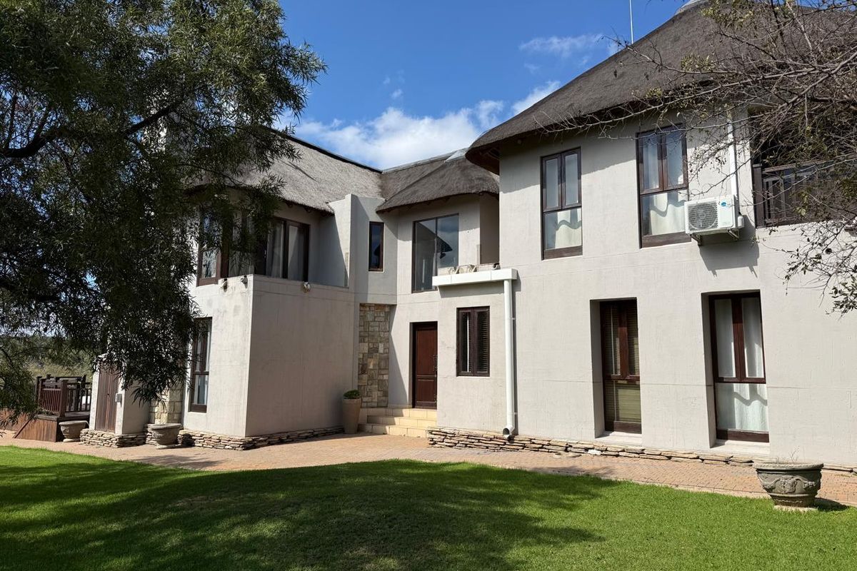Rear elevation of a two-story house featuring a traditional thatched roof, stone accents, and a paved patio area overlooking the garden.