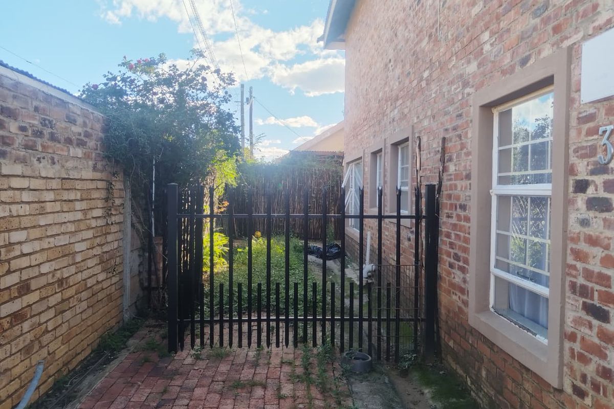 Side access path featuring brick paving, a secure metal gate, and exposed brick exterior walling of the townhouse.