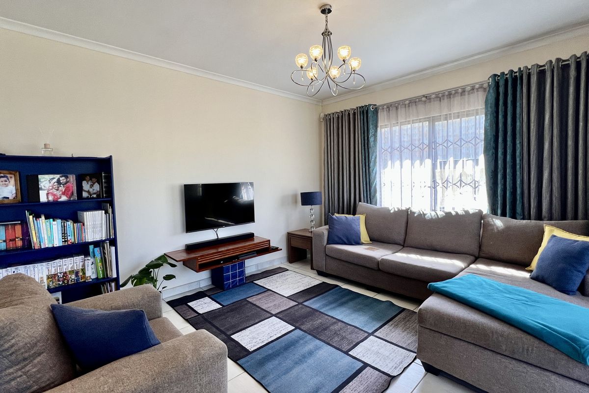 A comfortable living room featuring tiled flooring, a decorative chandelier, and large windows with security bars, providing a functional and well-lit space.