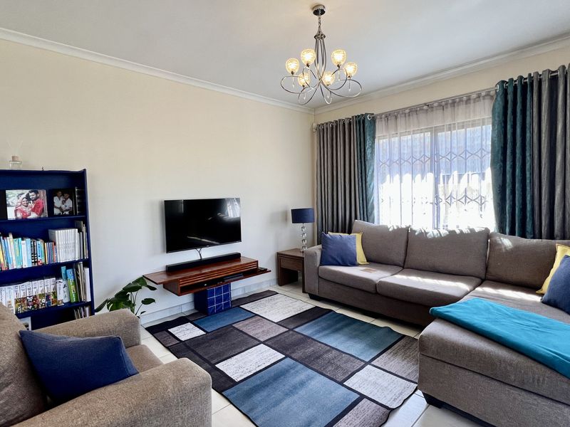 A comfortable living room featuring tiled flooring, a decorative chandelier, and large windows with security bars, providing a functional and well-lit space.