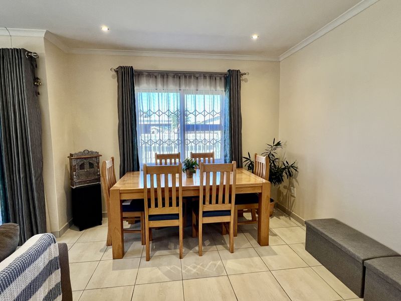 A bright dining area featuring neutral floor tiles, recessed ceiling lighting, and large windows with security gates.