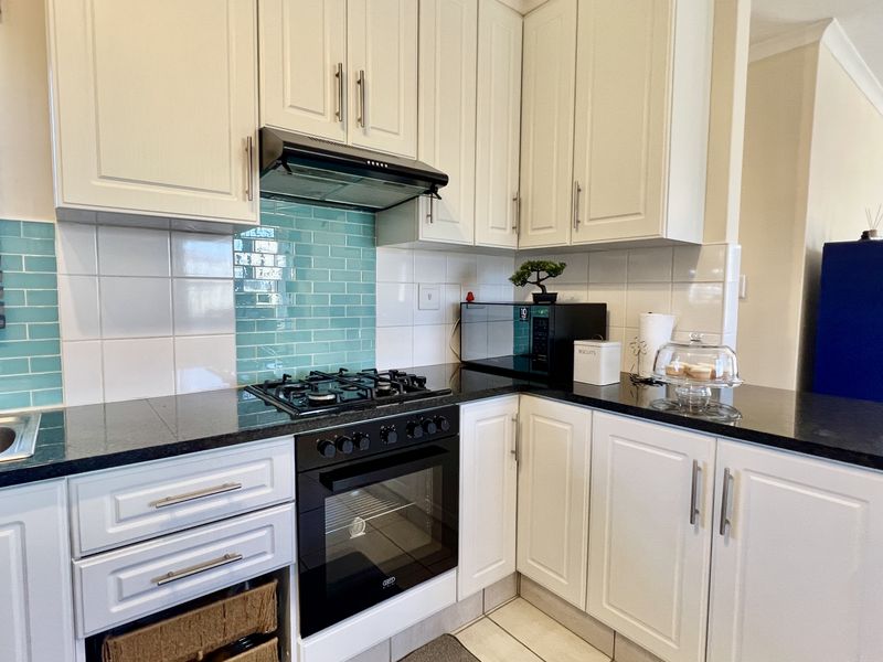 A well-maintained kitchen featuring white cabinetry, black granite countertops, a gas hob, built-in oven, extractor fan, and a vibrant turquoise tiled backsplash.