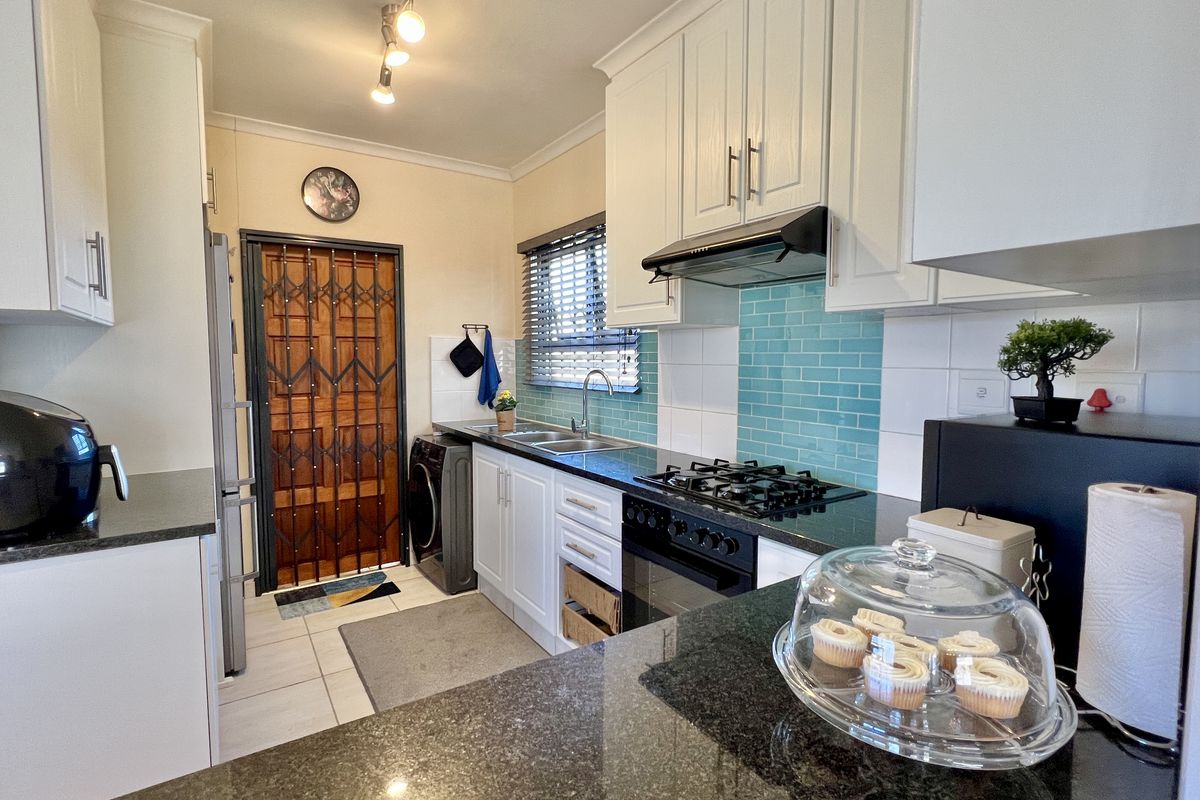 A functional kitchen featuring white cabinetry, dark granite countertops, a gas hob, extractor fan, and a vibrant teal subway tile backsplash.