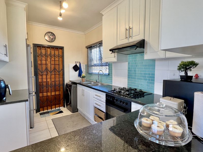 A functional kitchen featuring white cabinetry, dark granite countertops, a gas hob, extractor fan, and a vibrant teal subway tile backsplash.