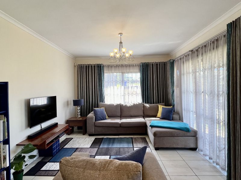 A comfortable living room featuring tiled flooring, large sliding glass doors with curtains, and a central chandelier, providing a bright and functional space.