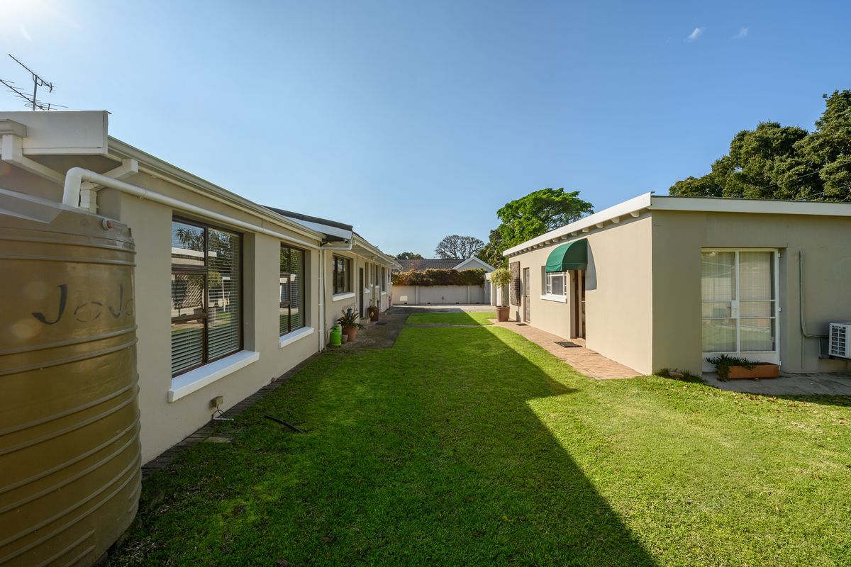 Rear exterior view of the property featuring a well-maintained lawn, paved pathways, and a water storage tank.