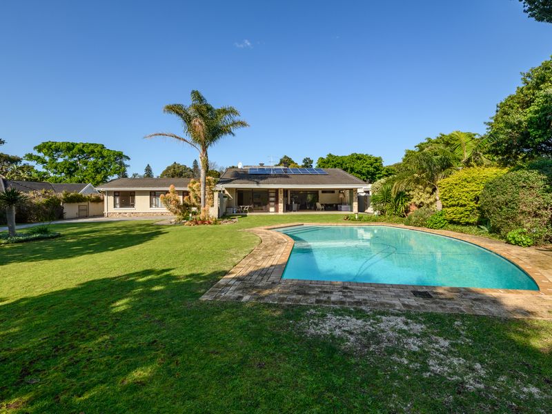 Spacious rear garden featuring a well-maintained swimming pool, paved surround, covered patio area, and solar panels installed on the tiled roof.