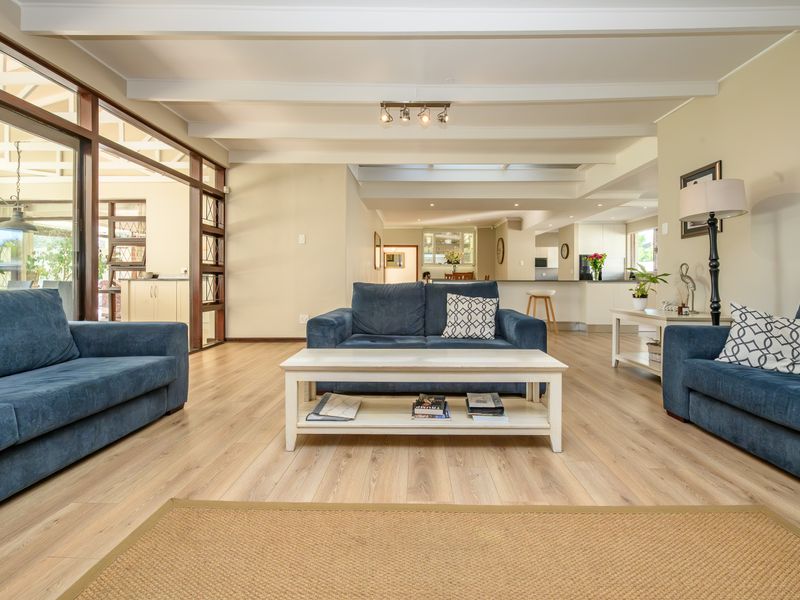 Spacious open-plan living area featuring light laminate flooring, exposed beam ceilings, and a seamless transition to the kitchen and outdoor patio space.