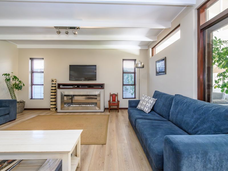 Spacious living room featuring exposed ceiling beams, laminate flooring, and a modern built-in fireplace, creating a bright and comfortable atmosphere.