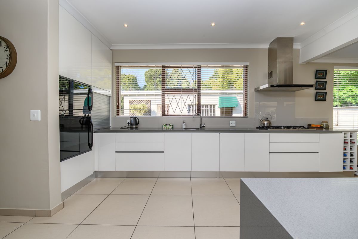 Modern kitchen featuring sleek white gloss cabinetry, stone countertops, integrated stainless steel appliances, gas hob, and tiled flooring with ample natural light.