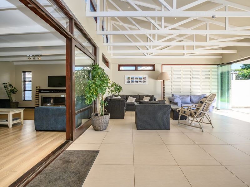 Spacious covered patio featuring exposed white timber roof trusses, large format floor tiles, and seamless indoor-outdoor flow through expansive sliding glass doors.