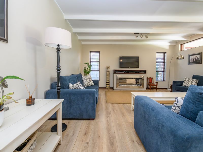 A bright and spacious living room featuring exposed ceiling beams, modern laminate flooring, and a central built-in fireplace.