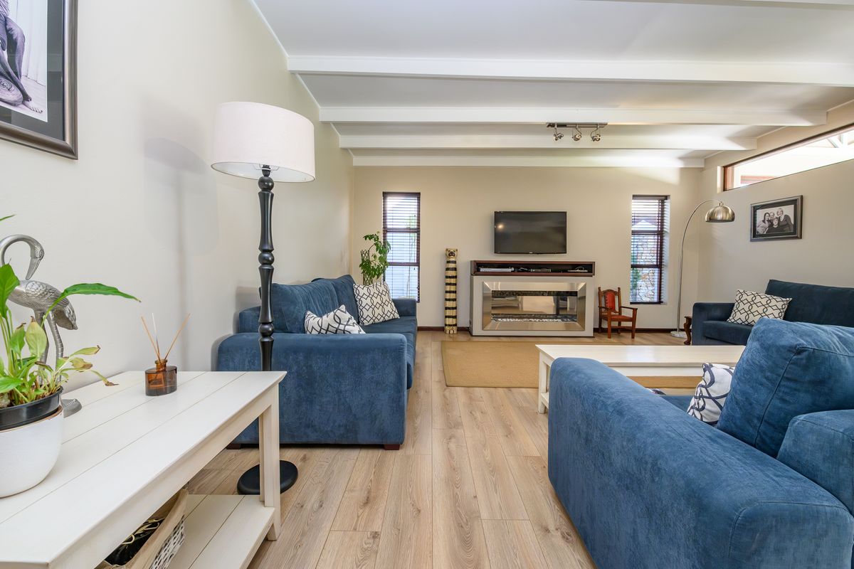 A bright and spacious living room featuring exposed ceiling beams, modern laminate flooring, and a central built-in fireplace.