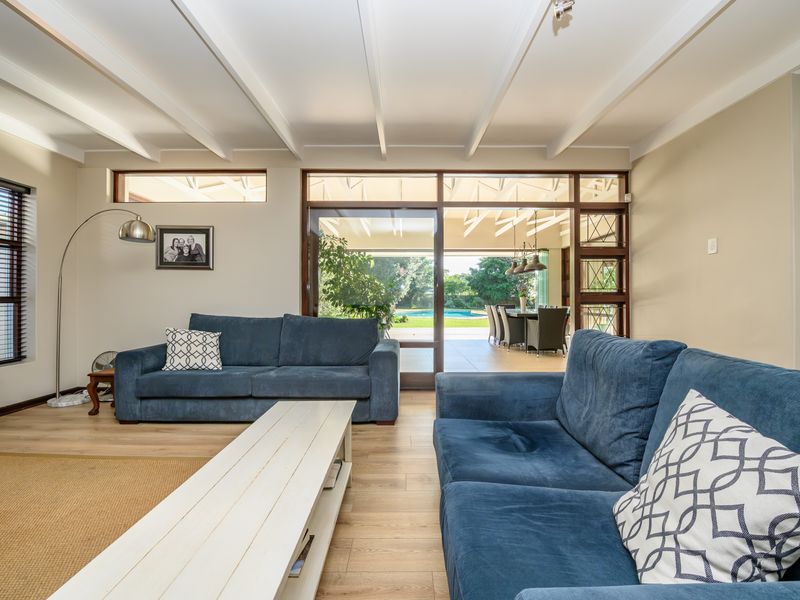 Spacious living room featuring exposed beam ceilings, laminate flooring, and large timber-framed sliding doors providing seamless access to the outdoor patio and pool area.