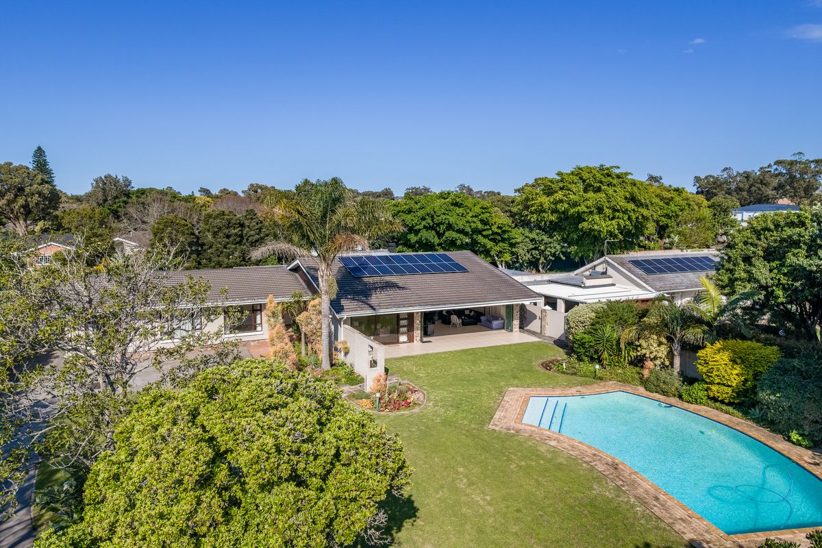 Aerial view of a spacious residential property featuring a large swimming pool, landscaped garden, covered patio, and roof-mounted solar panels.