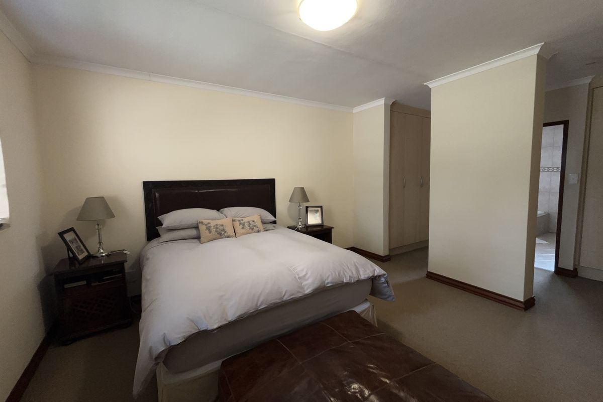 A spacious bedroom featuring neutral walls, carpeted flooring, coved cornicing, and built-in cupboards, with an adjoining en-suite bathroom area.