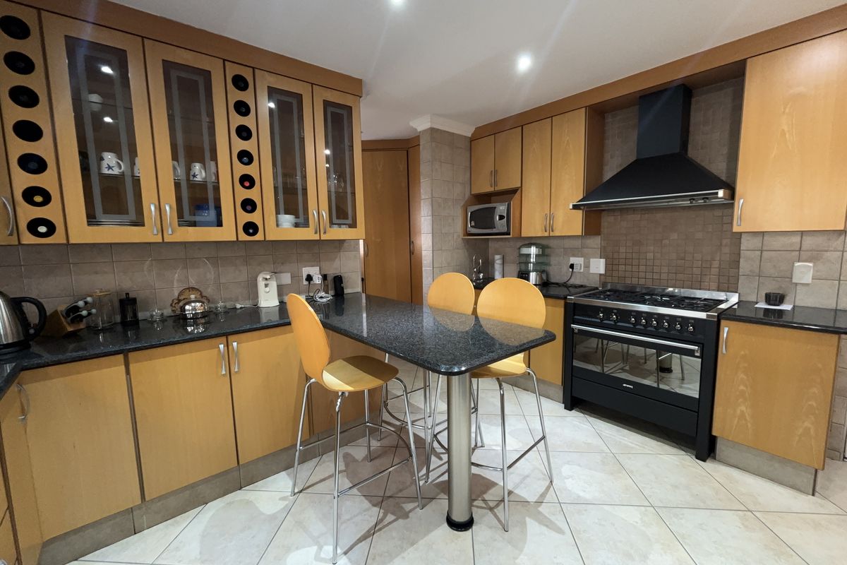 A functional kitchen featuring wooden cabinetry, granite countertops, a gas stove with extractor fan, and tiled flooring with an integrated breakfast bar.