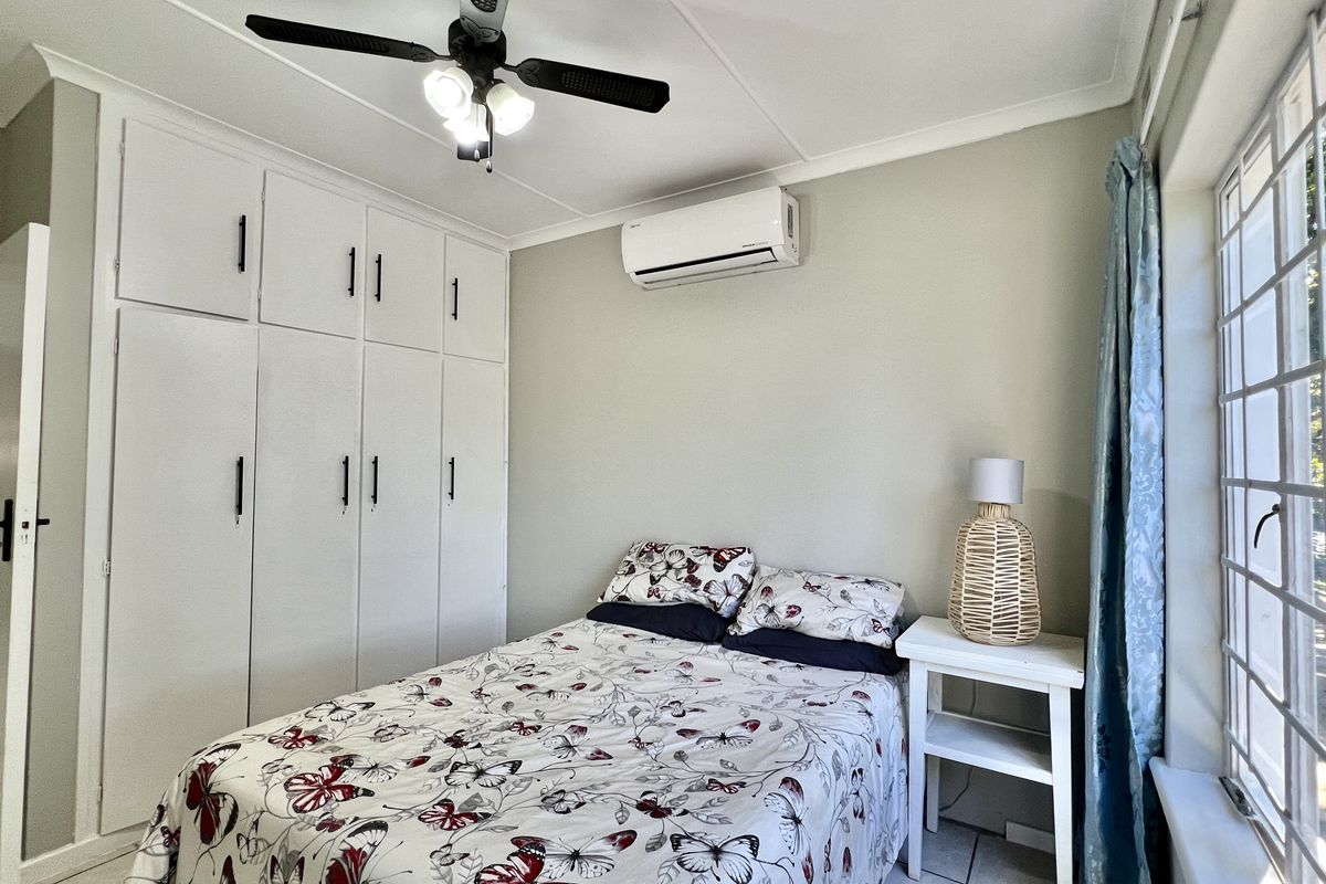 A well-maintained bedroom featuring built-in cupboards, a ceiling fan, and a split-system air conditioner for climate control.
