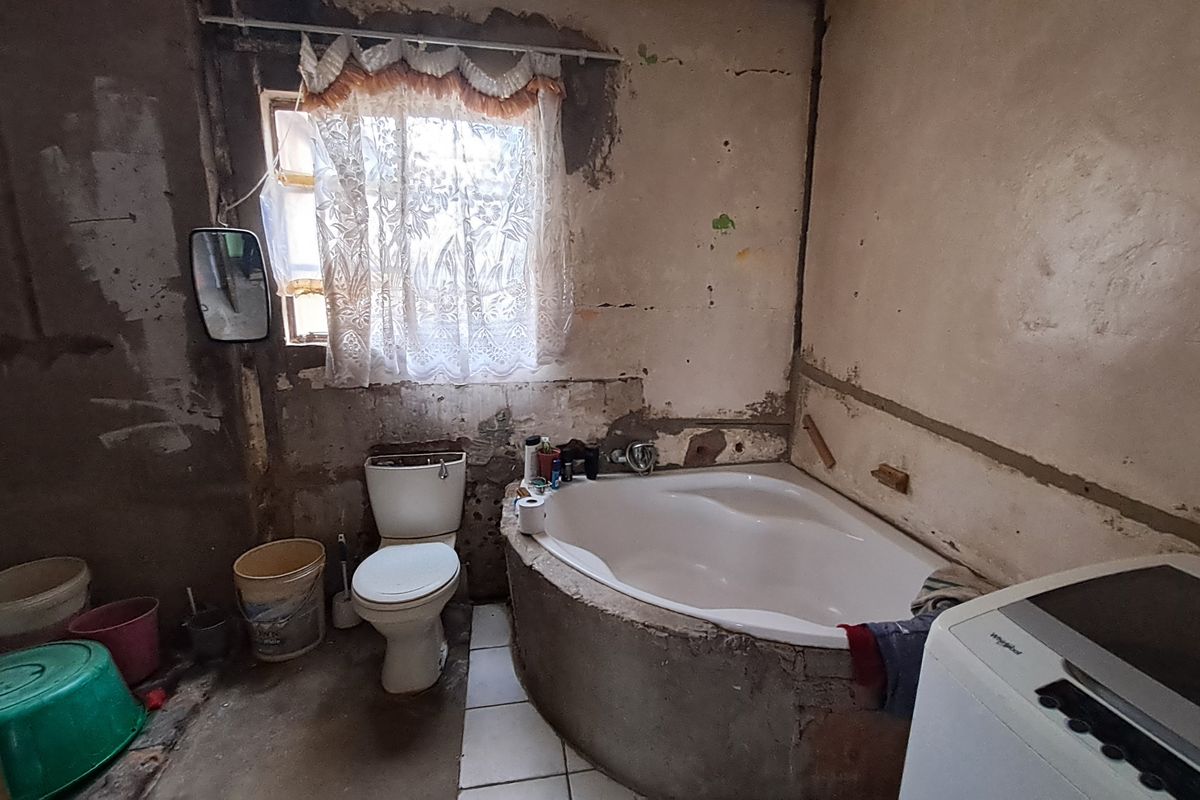 A bathroom in need of significant renovation, featuring a corner bathtub and toilet, with unfinished wall surfaces requiring plastering and cosmetic attention.
