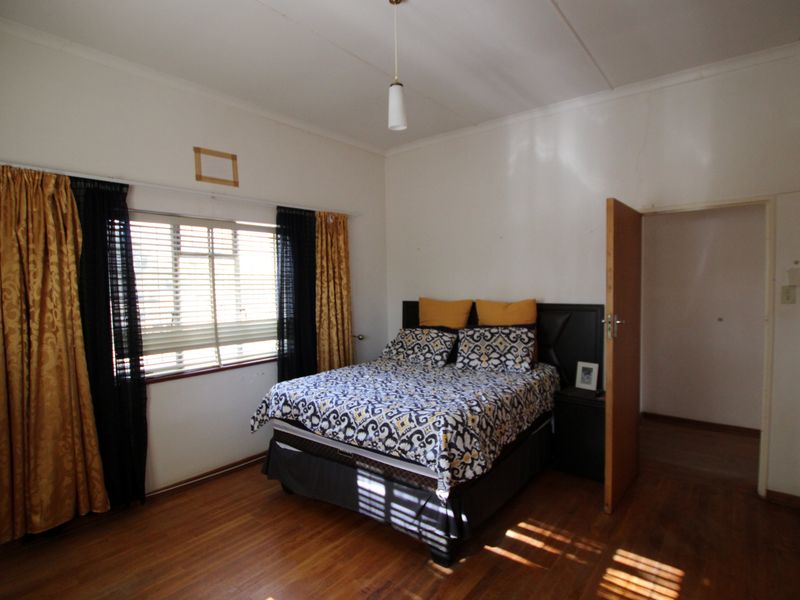 A bedroom featuring hardwood flooring, built-in cupboards, and natural light through venetian blinds.