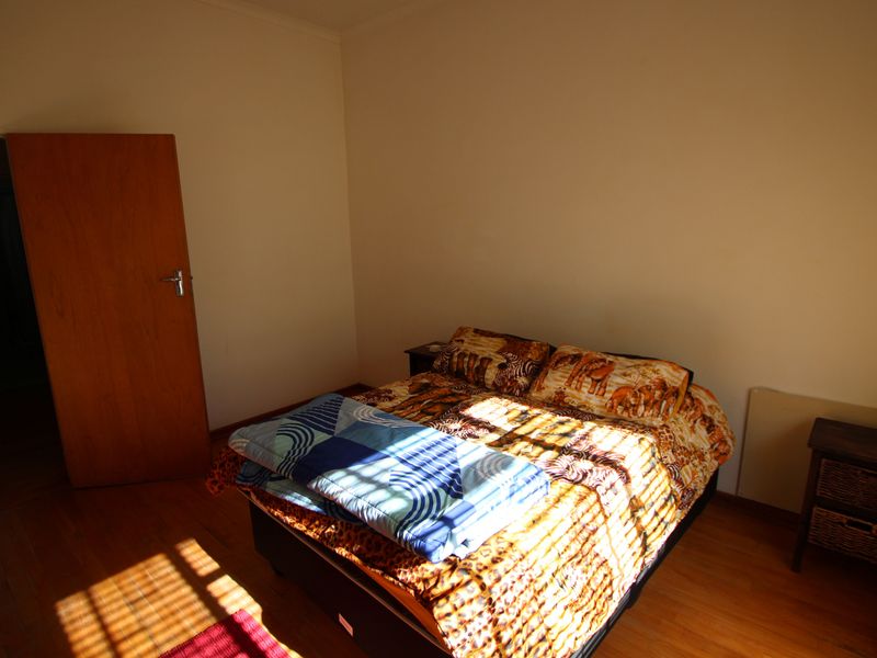 A bedroom featuring warm-toned wooden flooring and a solid core door, receiving natural light through window blinds.