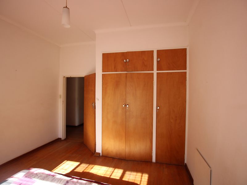 A bedroom featuring original hardwood flooring and built-in wooden cupboards, offering a blank canvas for potential updates.