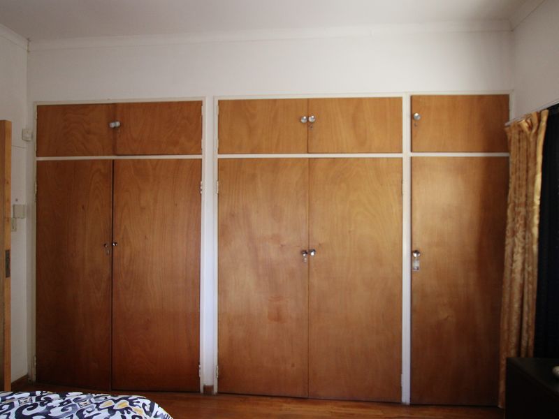 Bedroom featuring extensive floor-to-ceiling built-in wooden cupboards, polished wooden flooring, and an integrated air conditioning unit.