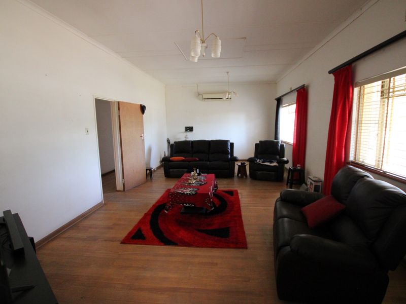 A spacious living room featuring laminate flooring, a wall-mounted air conditioning unit, and large windows with venetian blinds.
