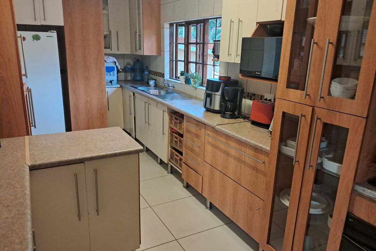 A functional kitchen featuring wood-tone and cream cabinetry, laminate countertops, tiled backsplash, and tiled flooring with ample storage space.