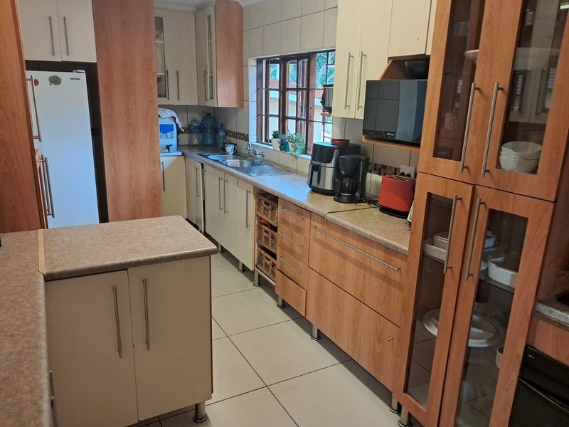 A functional kitchen featuring wood-tone and cream cabinetry, laminate countertops, tiled backsplash, and tiled flooring with ample storage space.