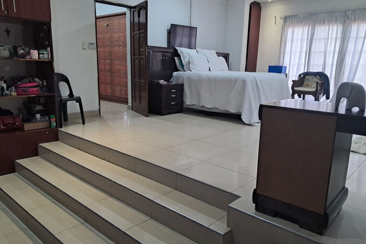 Spacious bedroom featuring a raised platform area, tiled flooring, and built-in cabinetry, with access to natural light through sliding glass doors.