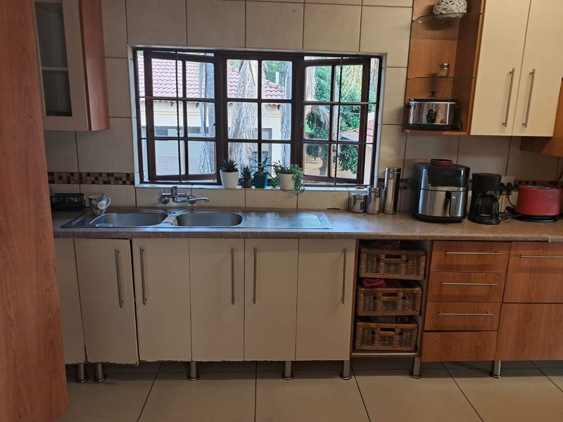 A functional kitchen area featuring a double bowl stainless steel sink, laminate countertops, tiled backsplash, and ample built-in cabinetry with a window view.