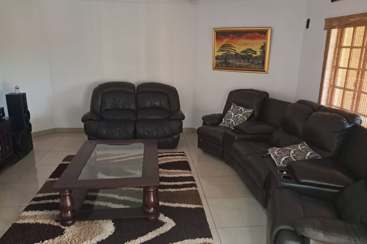 A spacious living room featuring neutral tiled flooring, coved cornicing, and a large window with a bamboo blind, offering a comfortable and functional living space.
